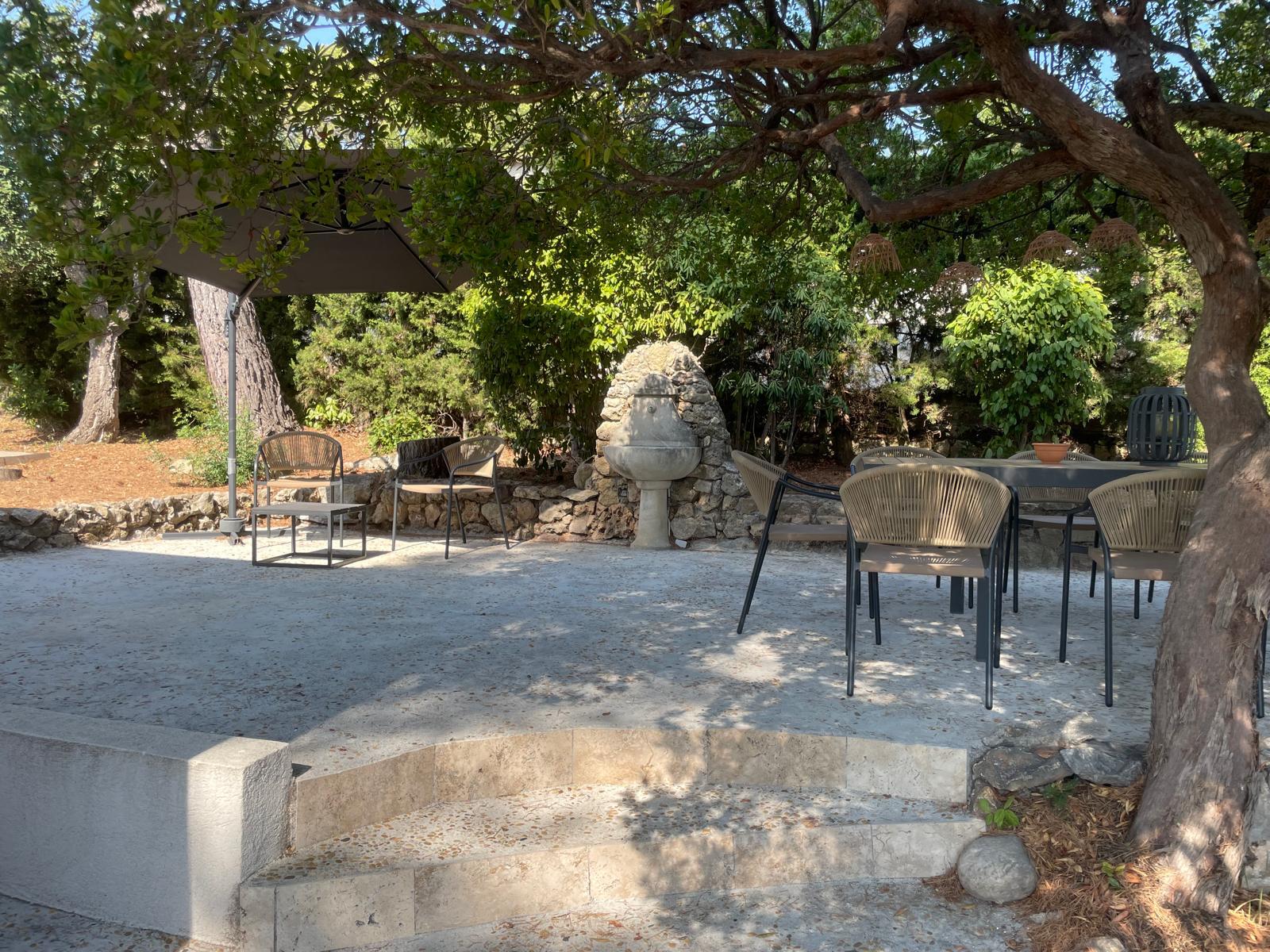Shaded garden terrace with dining table, lounge chairs and an old stone fountain