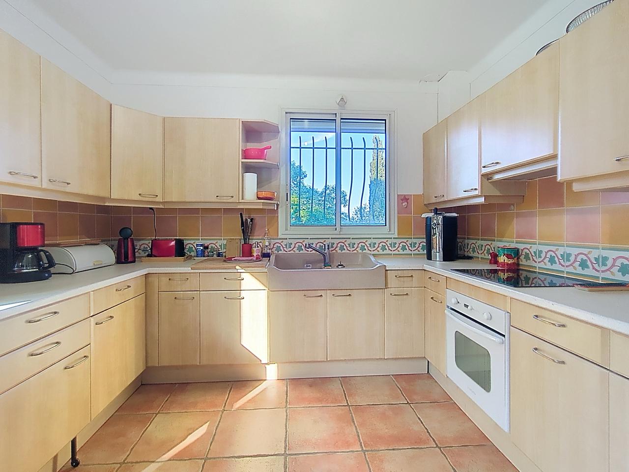 Kitchen with light wood cabinets, tiled backsplash and a window looking out onto the garden