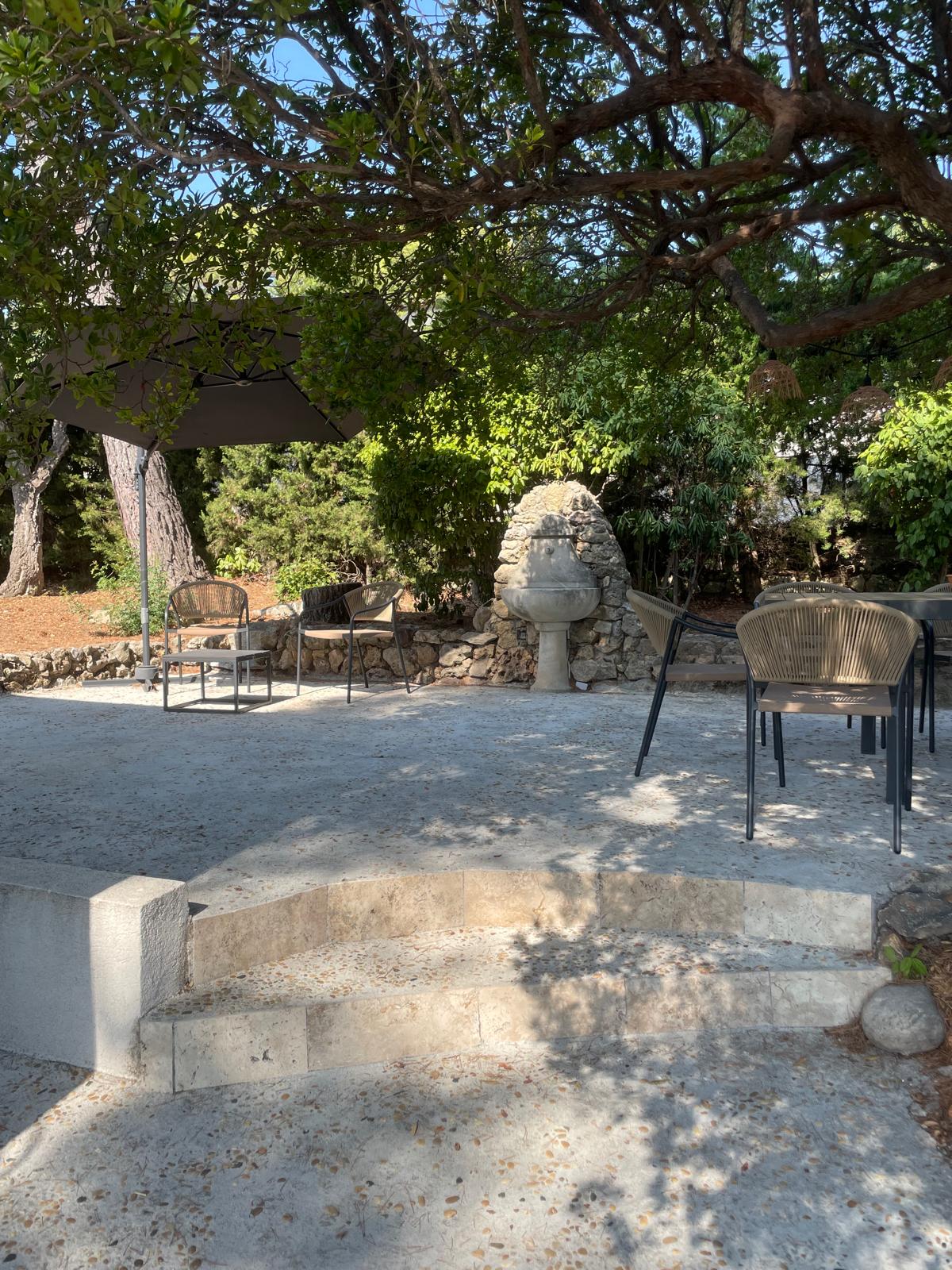 Shaded garden seating area with woven chairs beside an old stone fountain